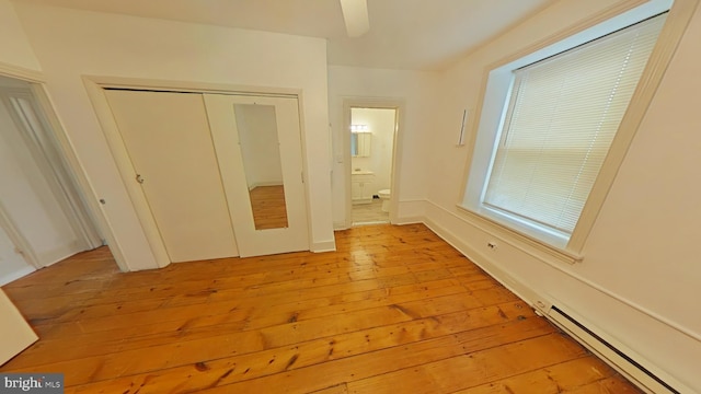 unfurnished bedroom with a baseboard heating unit, ensuite bath, a closet, and light wood-type flooring