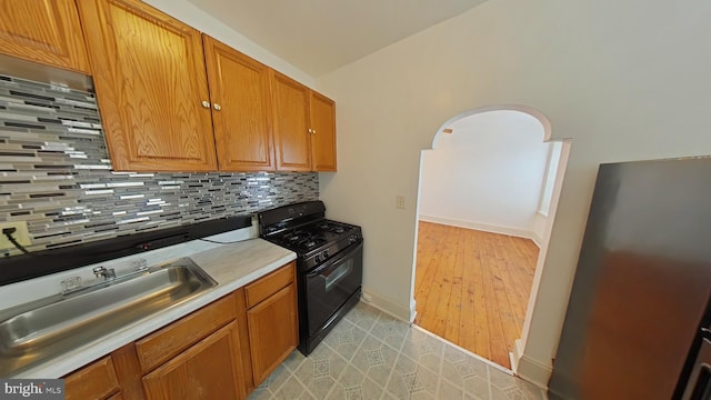 kitchen with backsplash, gas stove, sink, lofted ceiling, and light hardwood / wood-style floors