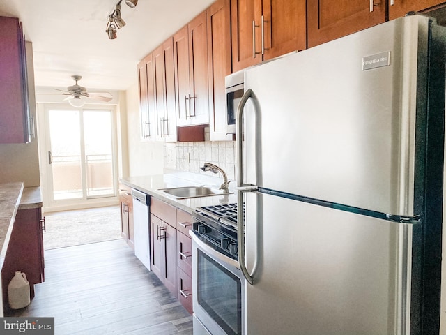 kitchen featuring decorative backsplash, gas range, sink, light hardwood / wood-style floors, and stainless steel refrigerator