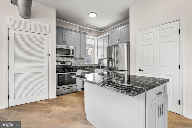 kitchen featuring light wood-type flooring, a center island, gray cabinetry, appliances with stainless steel finishes, and dark stone countertops