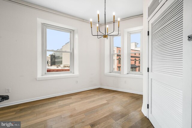 unfurnished dining area featuring wood-type flooring, an inviting chandelier, and crown molding