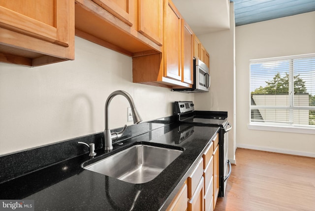 kitchen featuring a sink, baseboards, appliances with stainless steel finishes, dark stone counters, and light wood finished floors