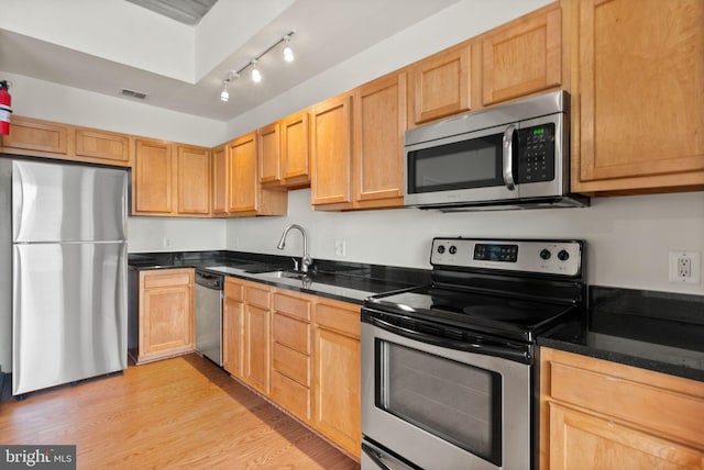 kitchen featuring a sink, visible vents, appliances with stainless steel finishes, light wood finished floors, and dark countertops