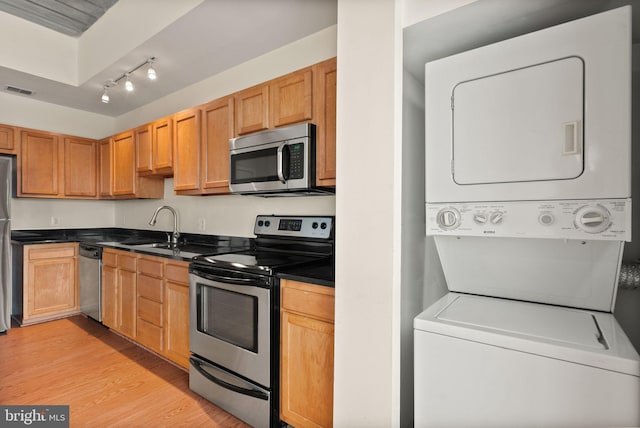 kitchen featuring dark countertops, stainless steel appliances, stacked washer and dryer, and a sink