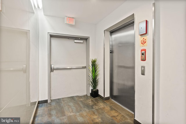 bathroom featuring elevator, stone finish flooring, and baseboards