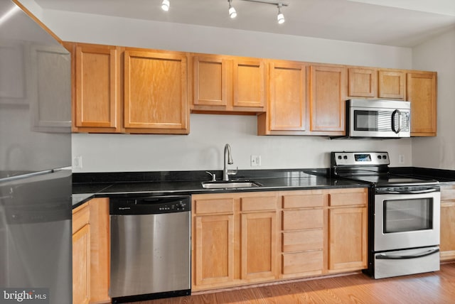 kitchen with sink, rail lighting, stainless steel appliances, light brown cabinets, and light hardwood / wood-style flooring