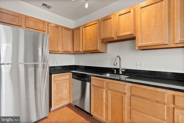 kitchen featuring a sink, visible vents, appliances with stainless steel finishes, light wood-type flooring, and dark stone counters