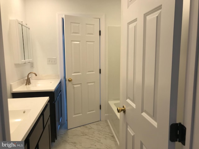 bathroom featuring marble finish floor, two vanities, a tub to relax in, and a sink