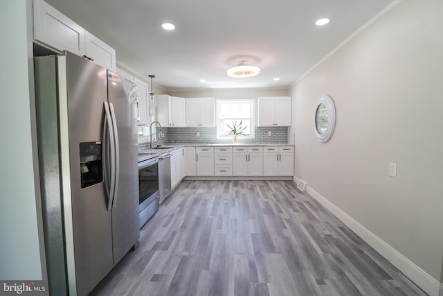 kitchen with light wood-type flooring, white cabinetry, decorative light fixtures, sink, and appliances with stainless steel finishes