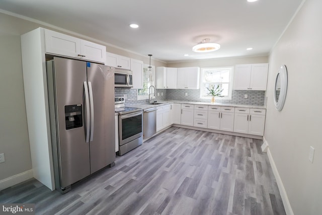 kitchen with pendant lighting, light hardwood / wood-style flooring, stainless steel appliances, and white cabinets