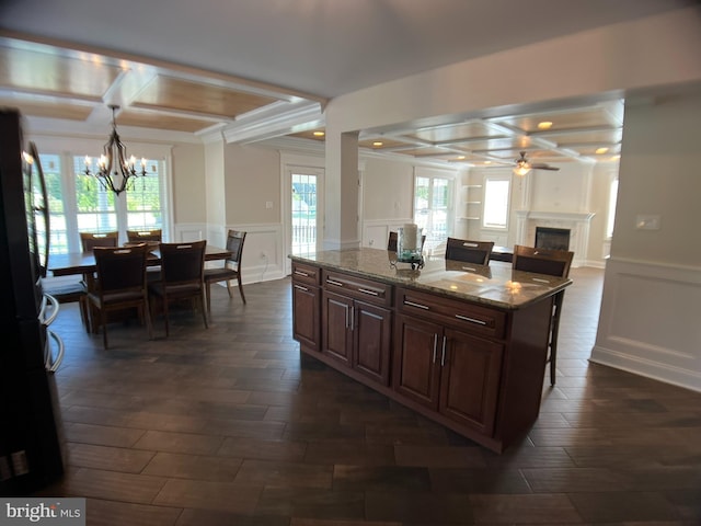 kitchen with dark stone counters, coffered ceiling, decorative light fixtures, and dark wood-type flooring