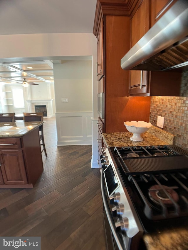 kitchen with gas range, dark hardwood / wood-style floors, stone countertops, extractor fan, and decorative backsplash