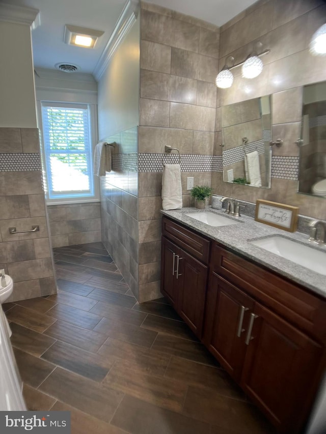 bathroom with toilet, tile walls, wood-type flooring, vanity, and ornamental molding