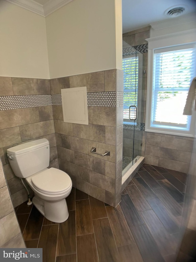 bathroom featuring crown molding, tile walls, toilet, and a shower with door