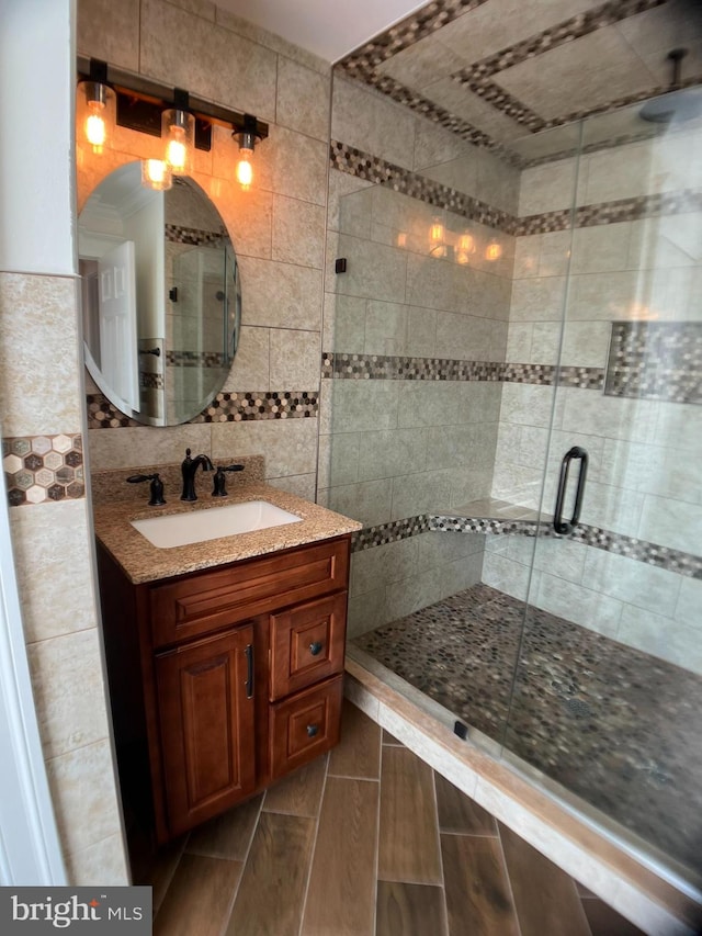 bathroom featuring a shower with door, vanity, wood-type flooring, and tile walls