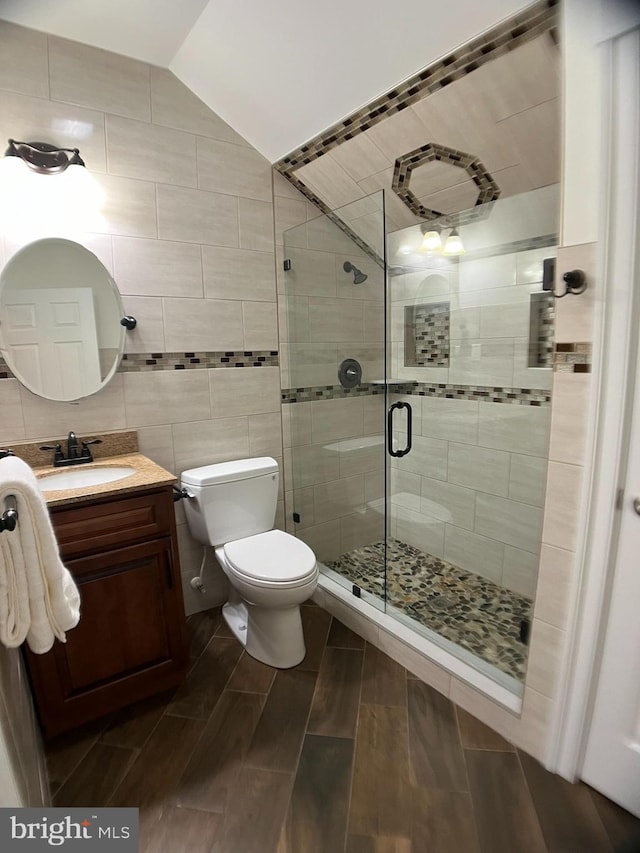 bathroom with vanity, vaulted ceiling, walk in shower, tile walls, and toilet