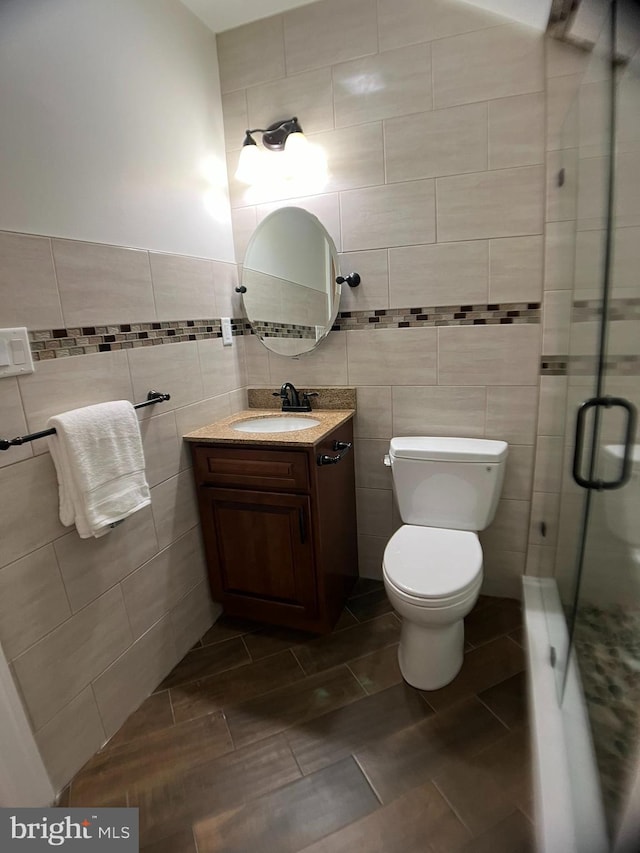 bathroom featuring tile walls, a shower with shower door, toilet, and vanity