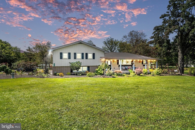 back of house at dusk with a lawn and brick siding