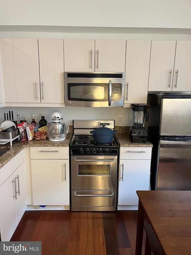 kitchen with white cabinets, dark stone countertops, stainless steel appliances, and dark hardwood / wood-style floors