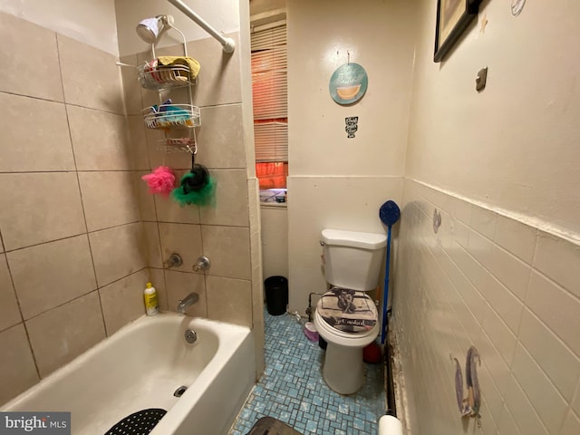 bathroom with tile walls, toilet, tile patterned floors, and tiled shower / bath