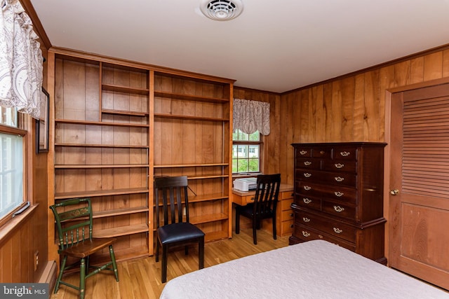 bedroom featuring crown molding, baseboard heating, wooden walls, and light hardwood / wood-style floors