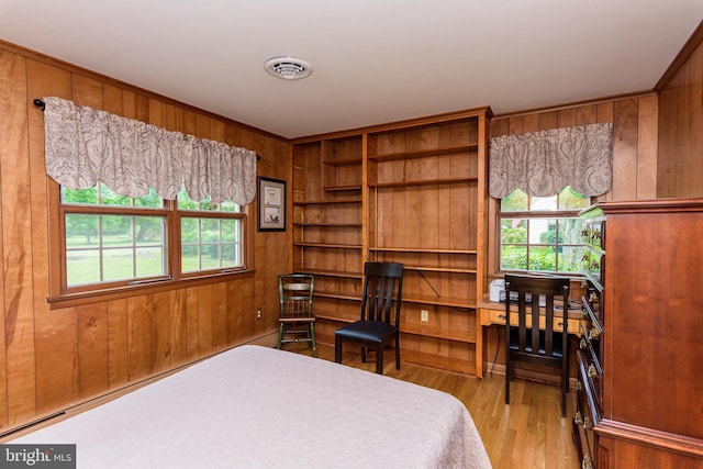 bedroom with multiple windows, light hardwood / wood-style floors, and wood walls