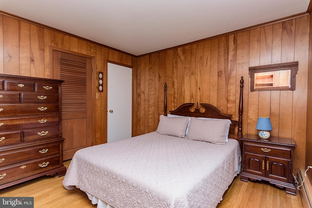 bedroom with light wood-type flooring, a baseboard heating unit, wooden walls, and a closet