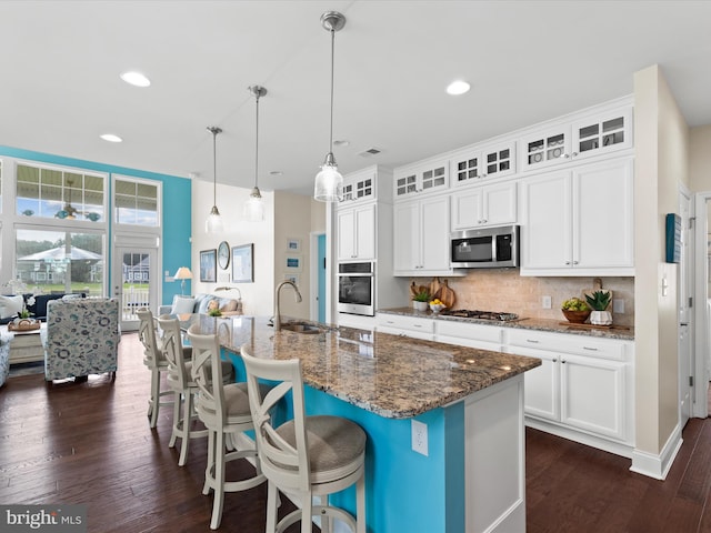 kitchen with an island with sink, decorative light fixtures, white cabinetry, stainless steel appliances, and dark hardwood / wood-style floors