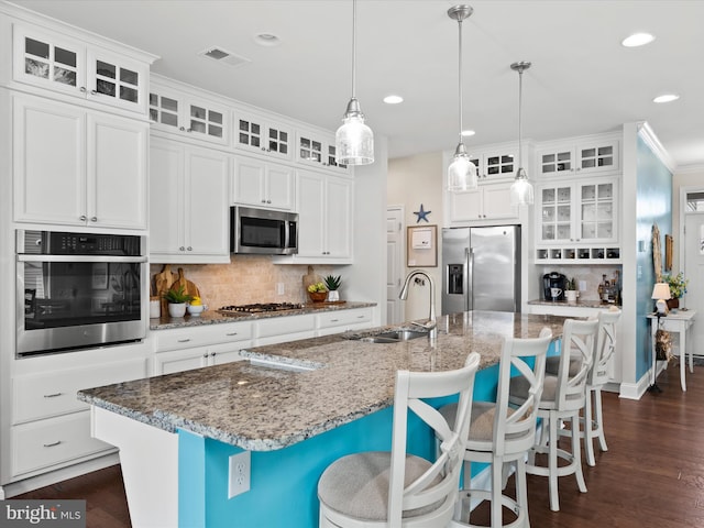 kitchen with a kitchen island with sink, pendant lighting, stainless steel appliances, and white cabinets