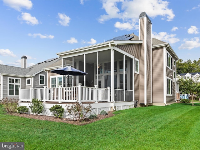 rear view of house featuring a deck, a sunroom, and a lawn