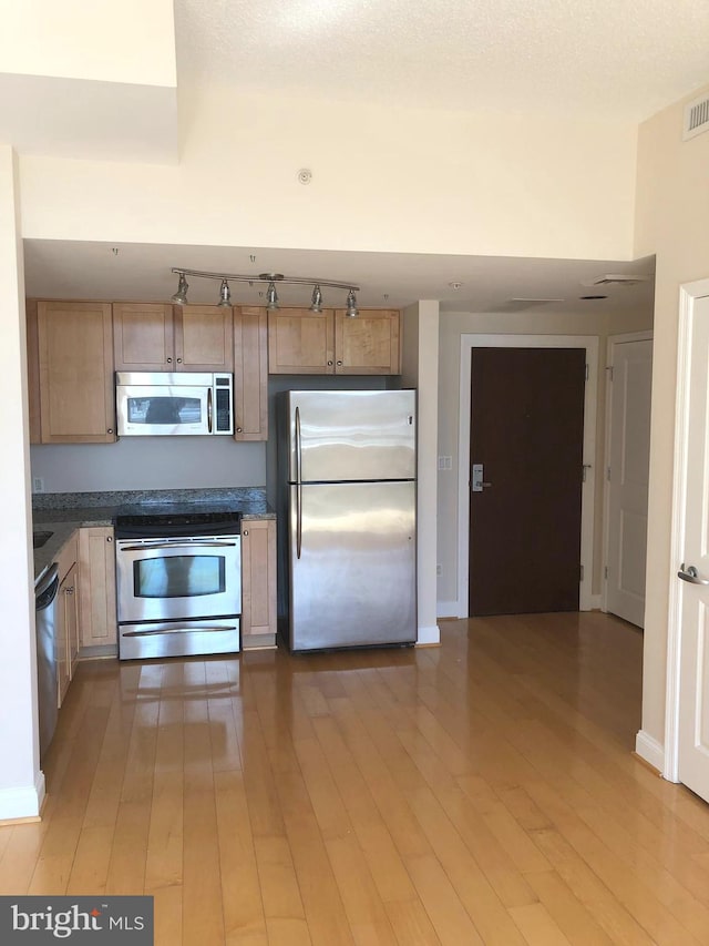 kitchen featuring stainless steel appliances, light wood finished floors, dark countertops, and baseboards