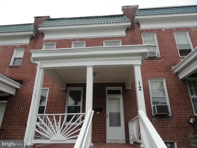 view of exterior entry with brick siding, a tiled roof, and mansard roof