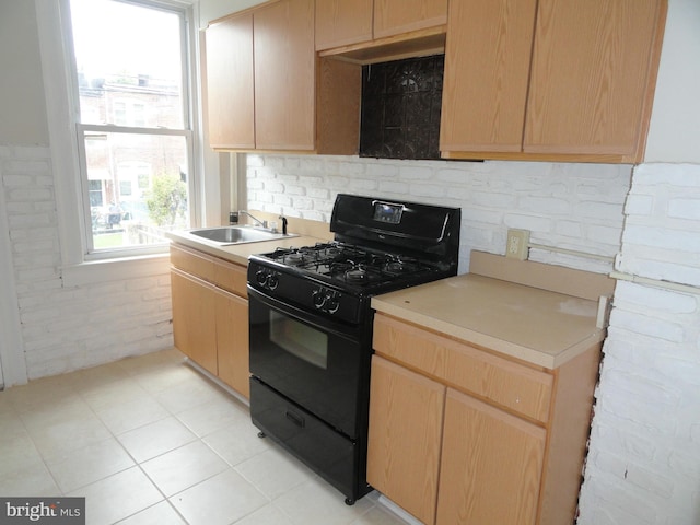 kitchen featuring brick wall, light brown cabinetry, light tile patterned floors, sink, and black gas range oven