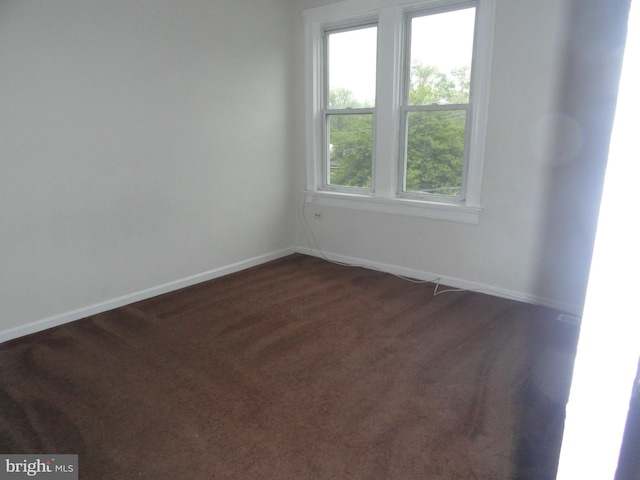 spare room featuring plenty of natural light and dark colored carpet