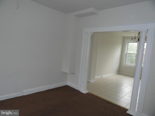 tiled spare room with decorative columns, baseboards, and a chandelier