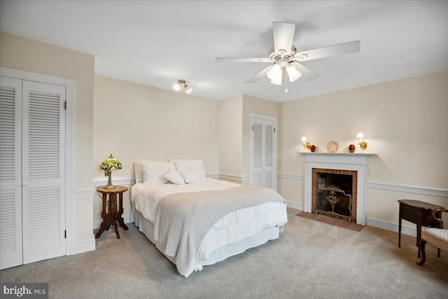 carpeted bedroom with multiple closets, ceiling fan, and a fireplace