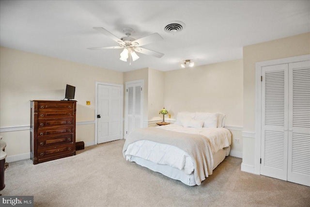 carpeted bedroom with ceiling fan and multiple closets