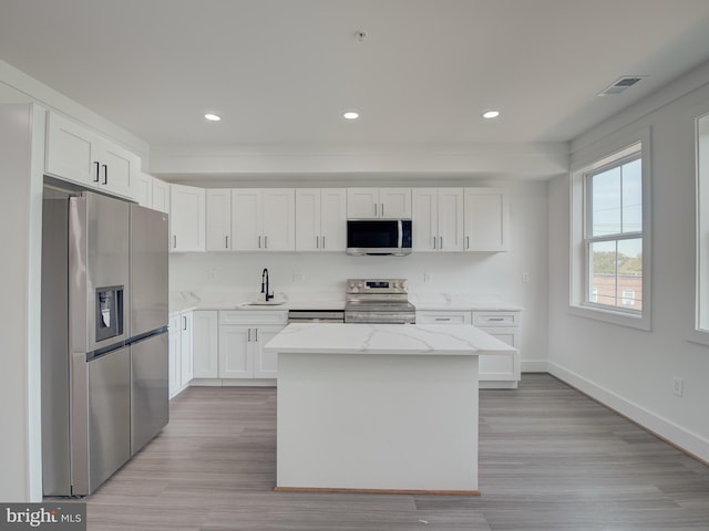 kitchen with light wood-type flooring, white cabinets, appliances with stainless steel finishes, and a kitchen island