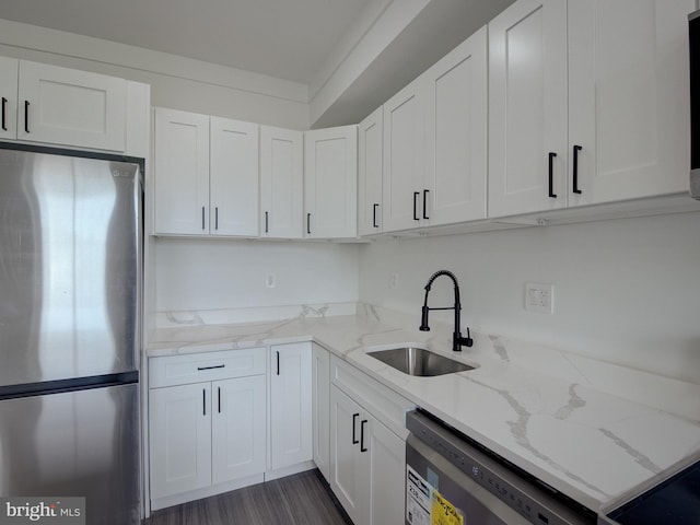 kitchen featuring appliances with stainless steel finishes, white cabinetry, light stone counters, and sink