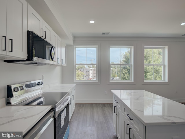 kitchen with white cabinets, a center island, light hardwood / wood-style flooring, light stone counters, and stainless steel appliances