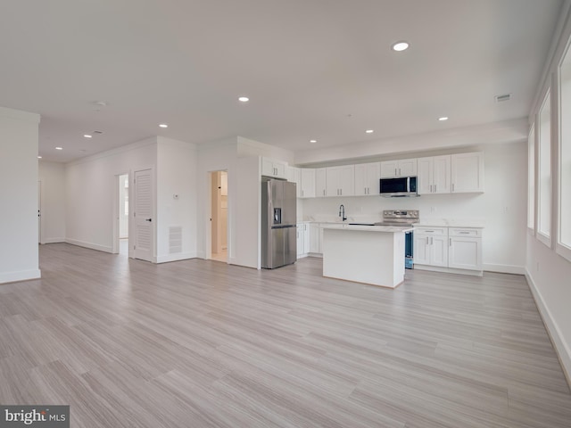 kitchen with white cabinets, appliances with stainless steel finishes, a kitchen island with sink, and light hardwood / wood-style flooring