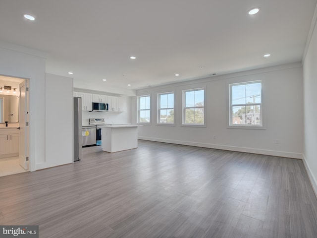 unfurnished living room with light wood-type flooring, a wealth of natural light, and crown molding