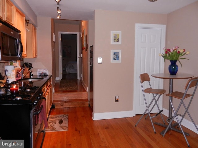 kitchen with light brown cabinets, black appliances, wood-type flooring, and sink