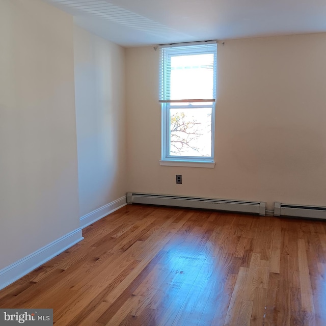 empty room with a baseboard radiator, light wood-style flooring, and baseboards