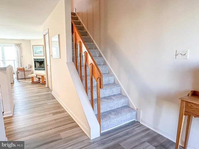 stairway with baseboards, wood finished floors, and a fireplace with raised hearth