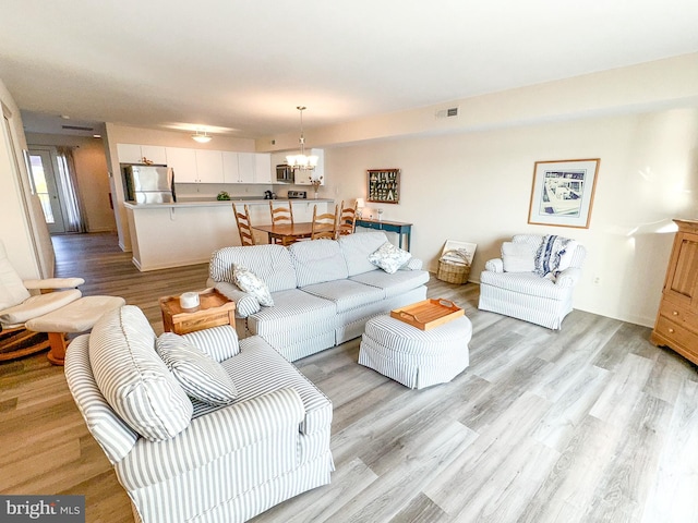 living area with light wood-style flooring, visible vents, and a chandelier