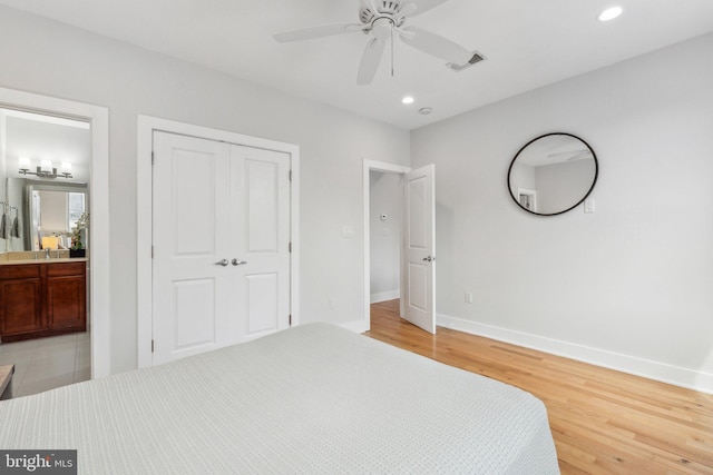 bedroom with light hardwood / wood-style flooring, a closet, ensuite bath, sink, and ceiling fan