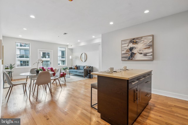 kitchen featuring light wood-type flooring, a kitchen island, dark brown cabinets, and a breakfast bar