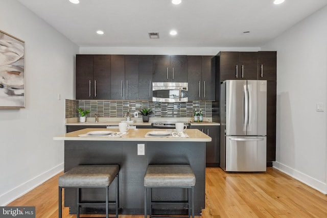 kitchen with a breakfast bar area, a kitchen island, stainless steel appliances, and light hardwood / wood-style floors