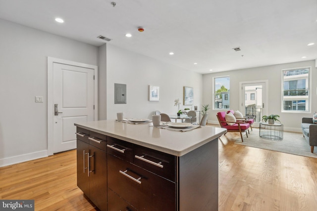 kitchen featuring light wood-type flooring, dark brown cabinets, a center island, and electric panel